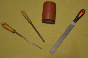 attrezzi per costruire una casetta in miniatura: tre tipi di lime e rotolo di carta abrasiva